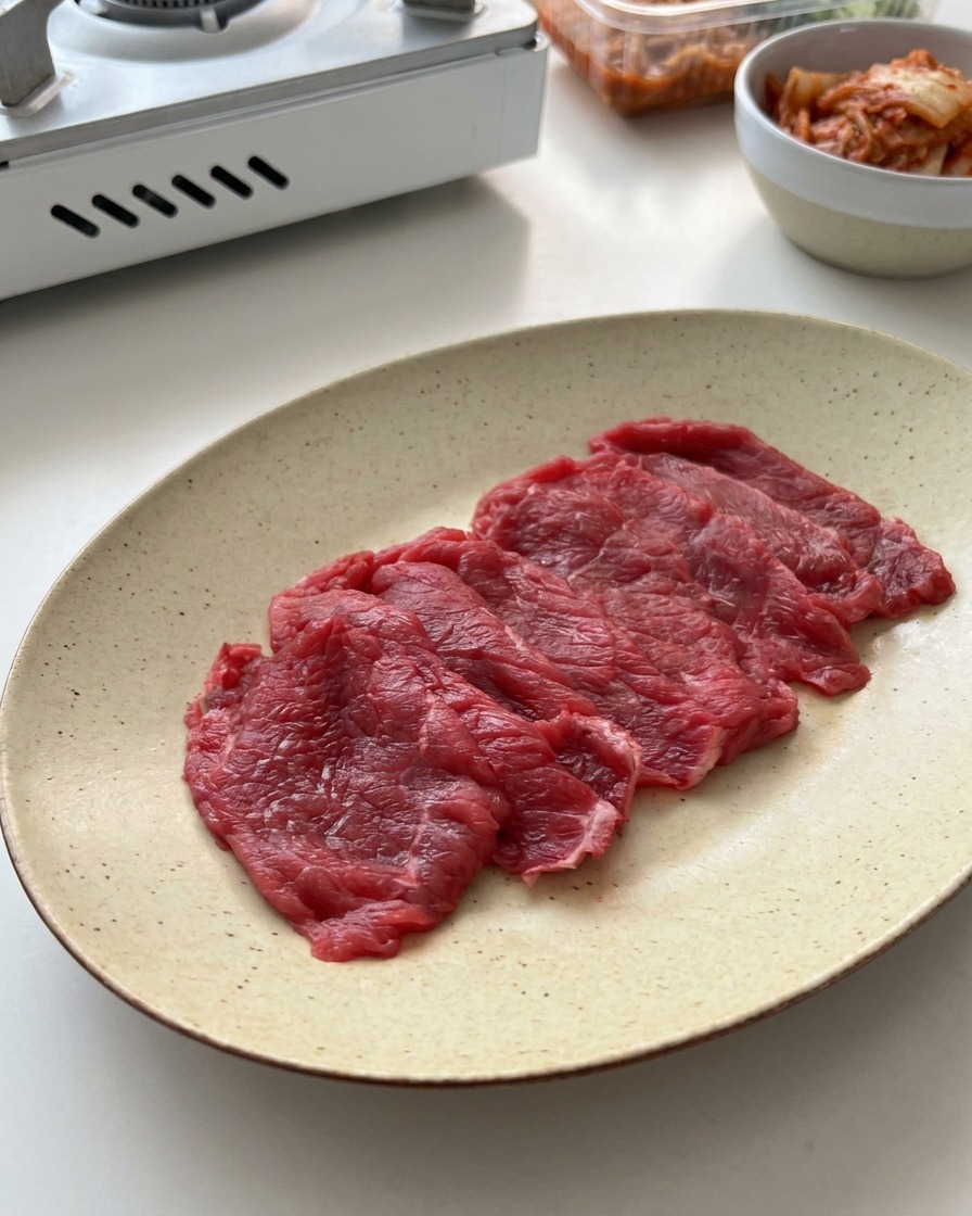 Thinly sliced raw beef laid out evenly on an off-white speckled ceramic plate.
