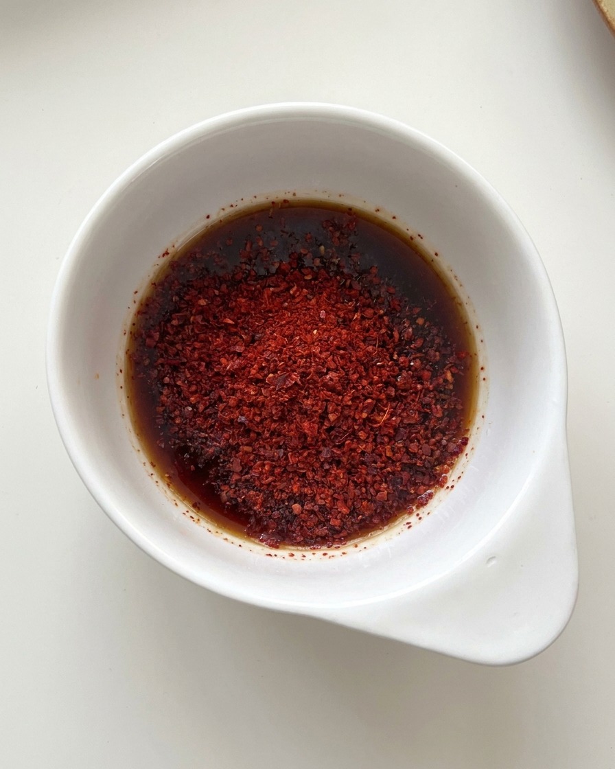 A small white bowl containing a mixture of dark soy sauce liquid and bright red chili powder.
