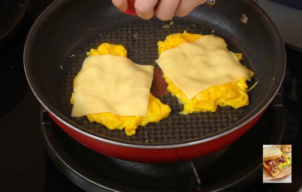 A person placing a bright red lid over a frying pan to trap steam and melt cheese on top of scrambled eggs.
