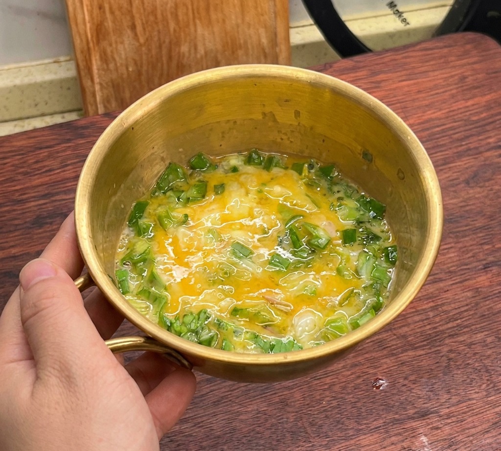 A mixture of beaten eggs and green lettuce combined in a golden bowl.