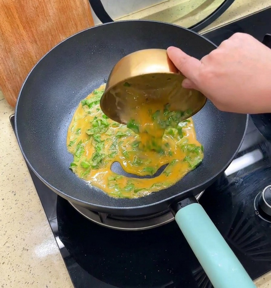 Whisked egg and shredded lettuce mixture being poured from a gold bowl into a black frying pan.