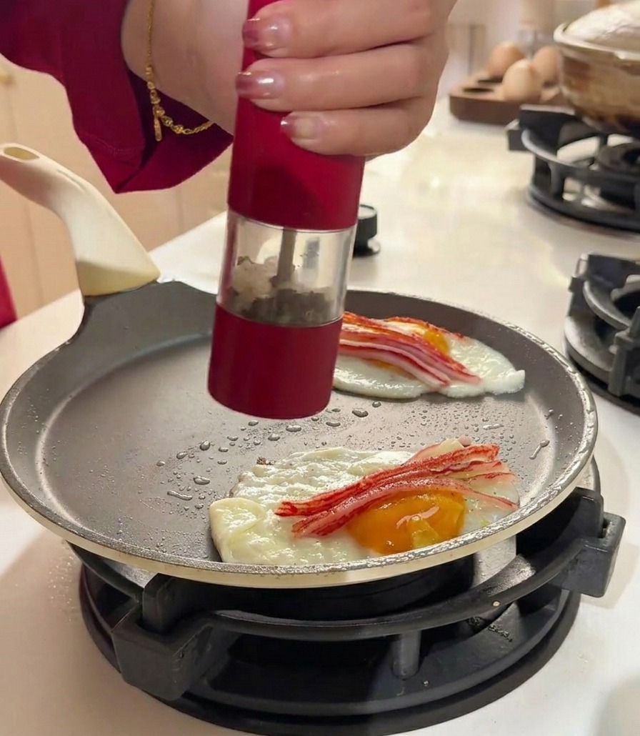 A red pepper grinder seasoning eggs and crab sticks in a flat frying pan.