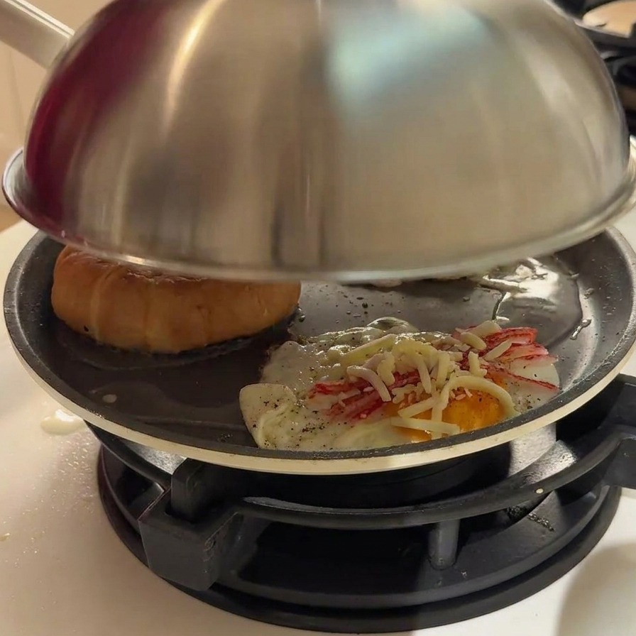 Steam rising from the edges of a metal lid covering a frying pan.