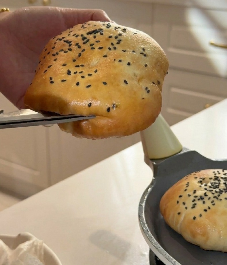 Using kitchen scissors to carefully slice the side of a fluffy burger bun to create a pocket for fillings.