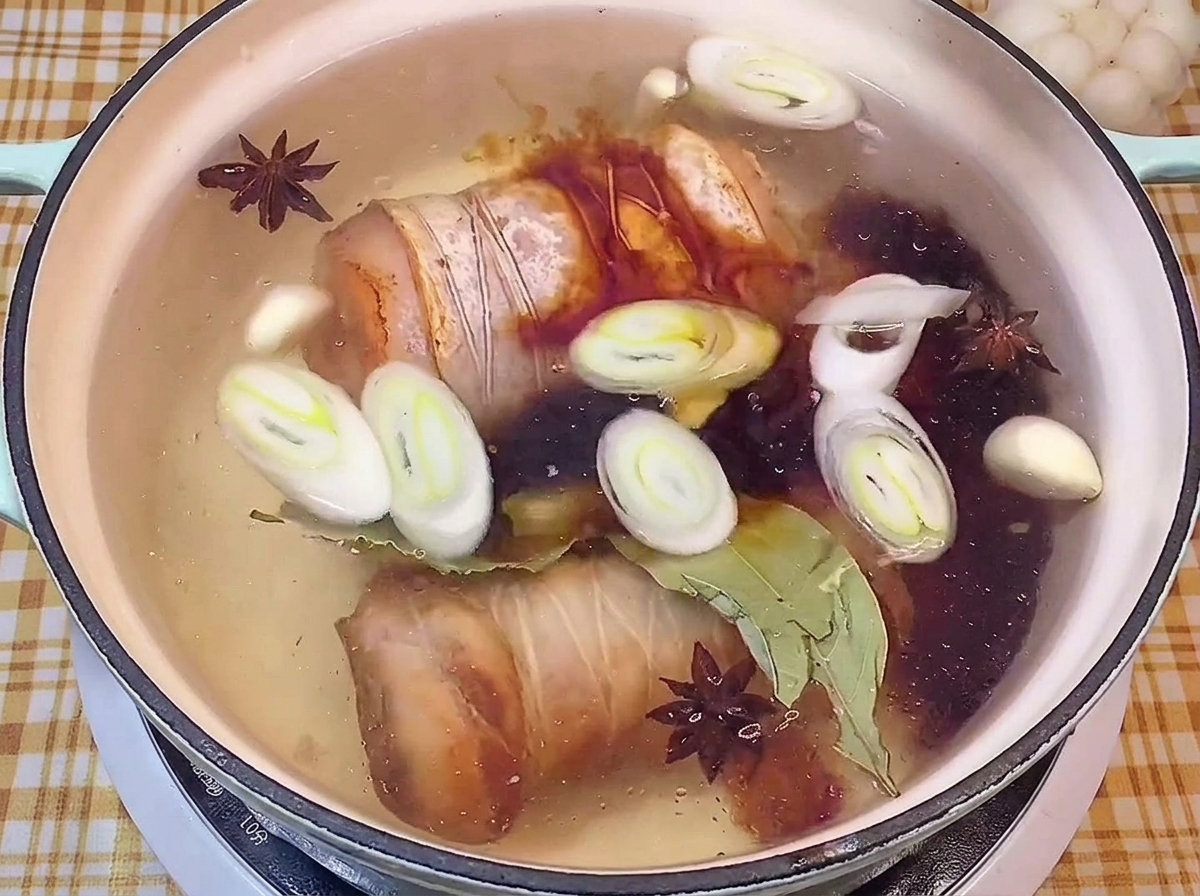 Adding dark soy sauce into a pot of braising liquid with pork belly rolls and spices.