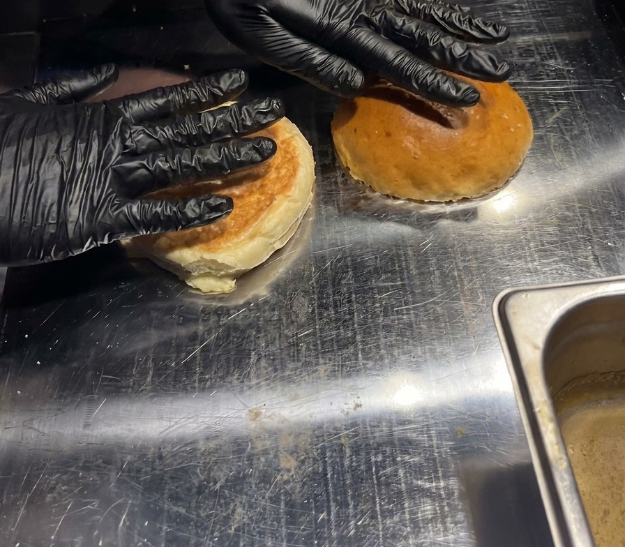 Two burger buns being pressed down by hand onto a hot metal griddle to toast the interiors.