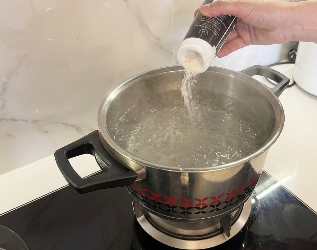 White salt being poured from a shaker into a pot of rapidly boiling water.
