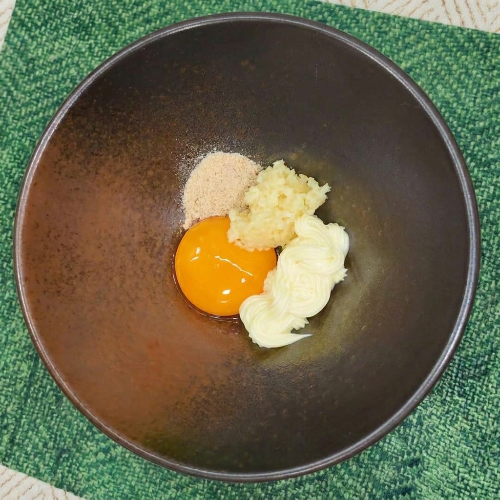 Instant noodle seasoning powder added to a bowl with egg yolk, garlic, and mayonnaise.