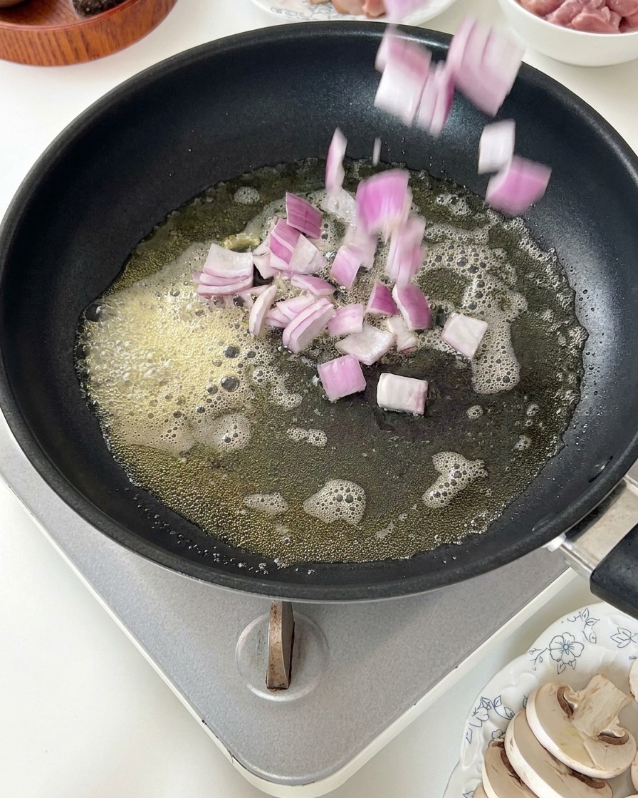 Diced red onions being dropped into a pan of foaming melted butter.