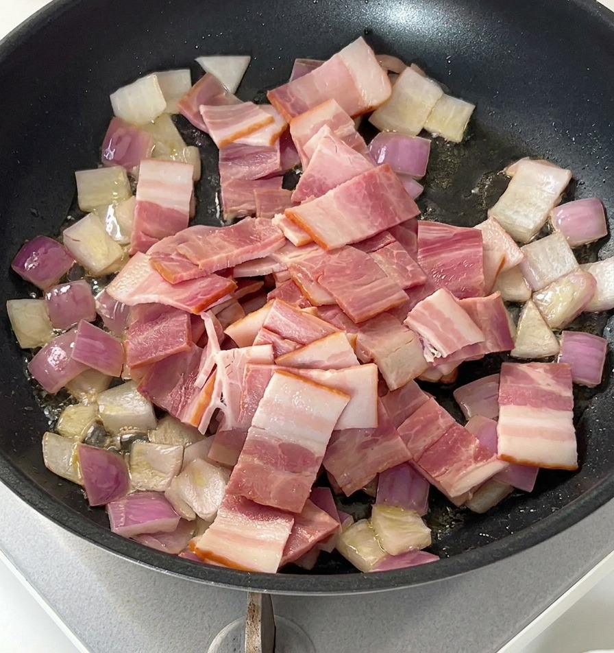 Raw sliced bacon pieces sitting on top of sautéed onions in a black frying pan.