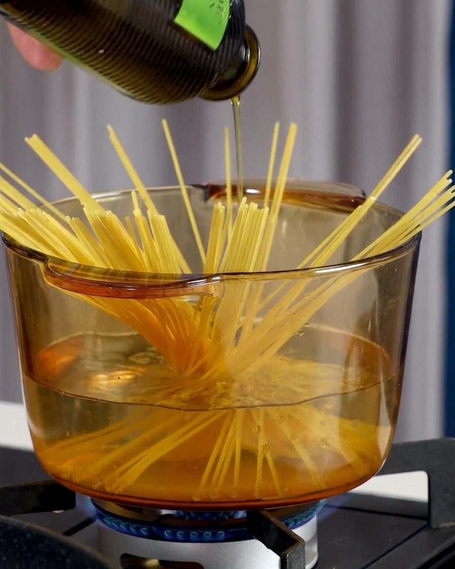 A hand sprinkling white sea salt into a clear pot of boiling water containing spaghetti strands.