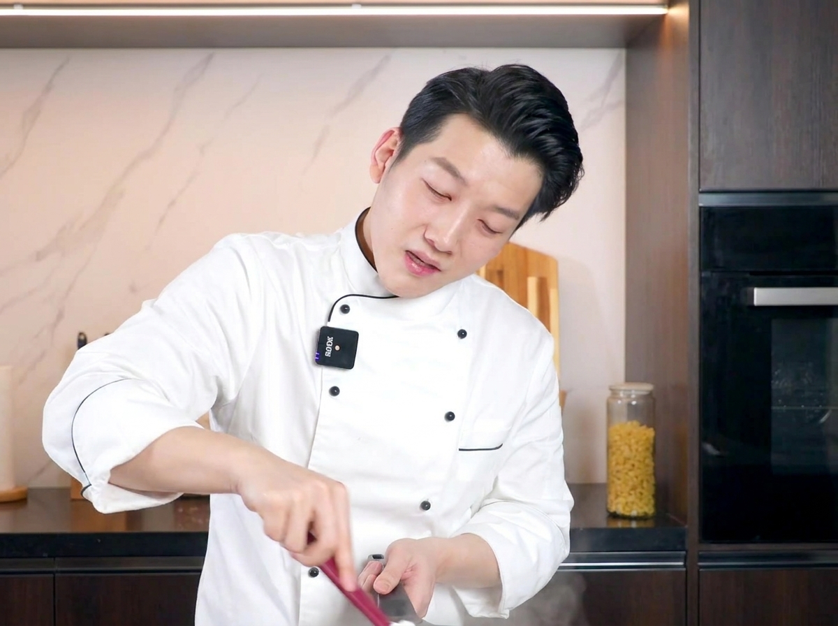A chef stirring a pan of creamy pasta with a red spatula, focusing on mixing the egg sauce into the noodles.