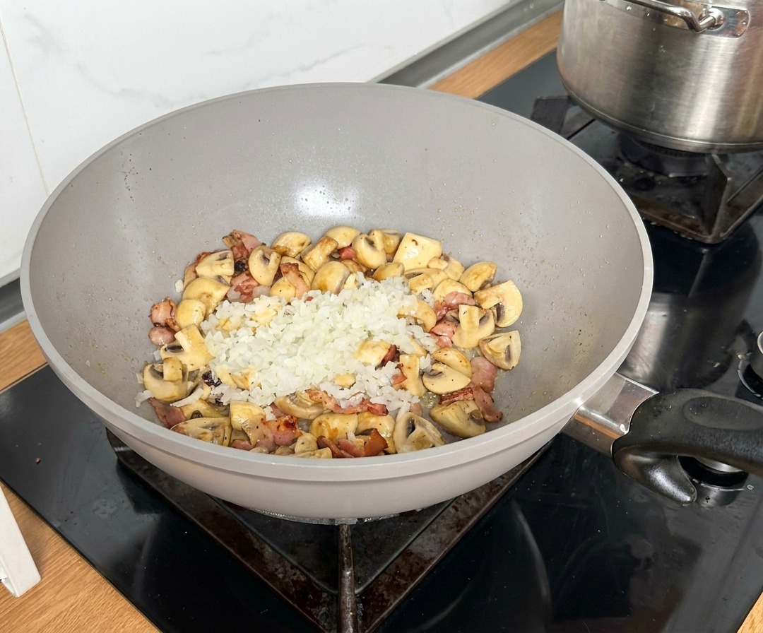 Diced onions placed in the center of a pan with browned bacon and mushrooms.
