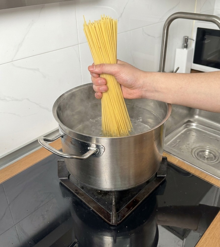 A bundle of dry spaghetti being placed into a stainless steel pot of boiling water.