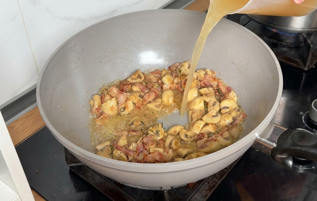 Chicken stock being poured from a clear plastic measuring cup into the skillet with the sautéed ingredients.