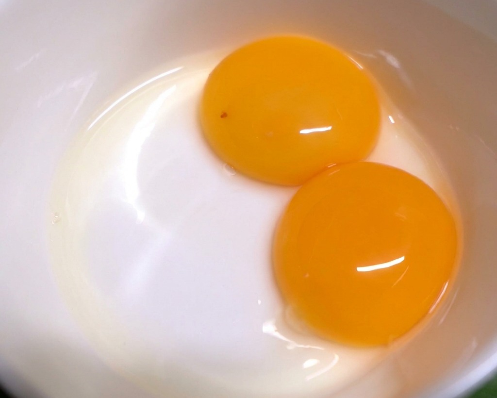 Three bright, intact egg yolks sitting at the bottom of a white ceramic bowl.