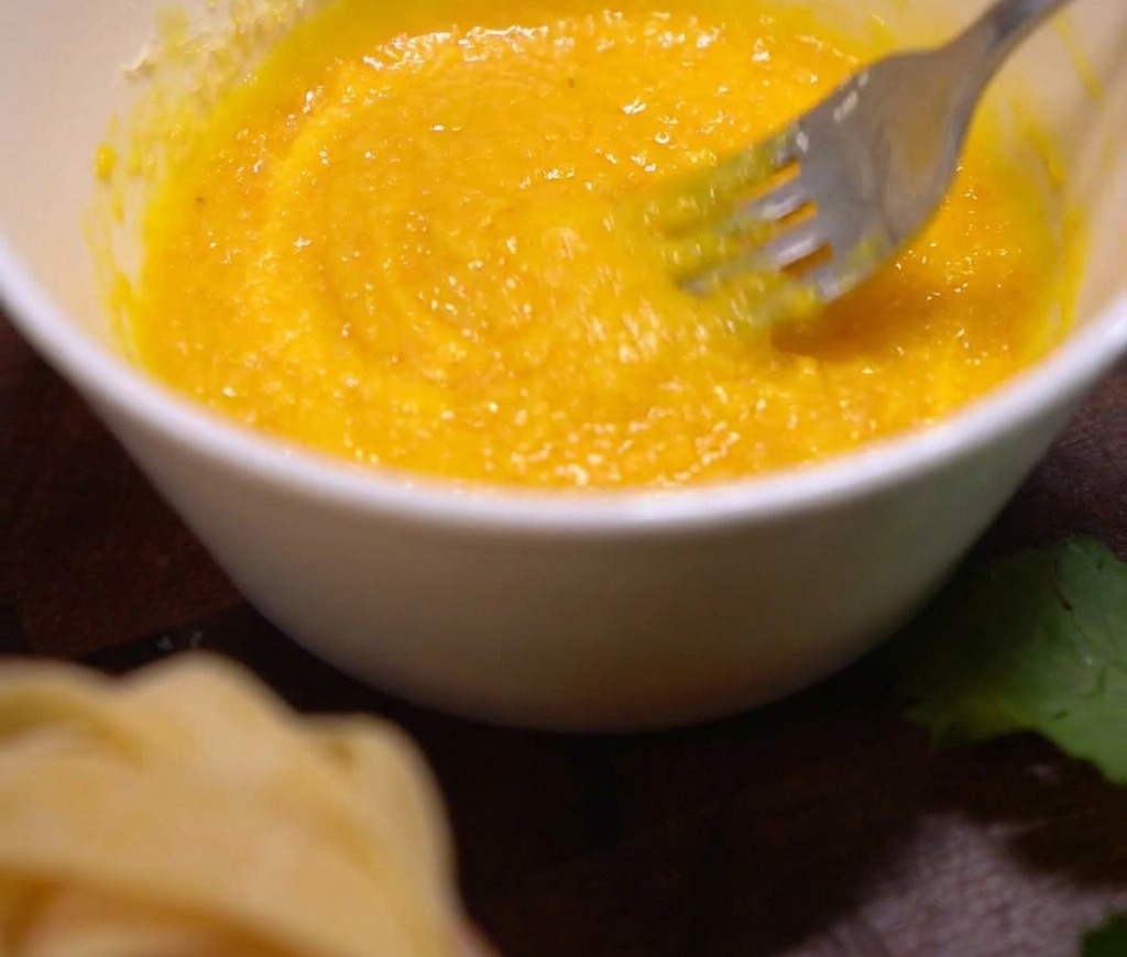 A white bowl containing egg yolks and grated Parmesan being mixed together with a metal fork.