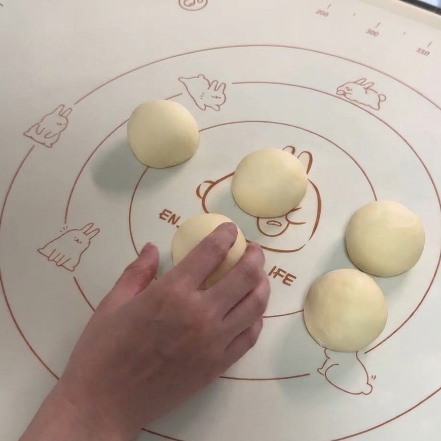 Six smooth, round dough balls arranged on a silicone baking mat with a hand rounding one of the portions.
