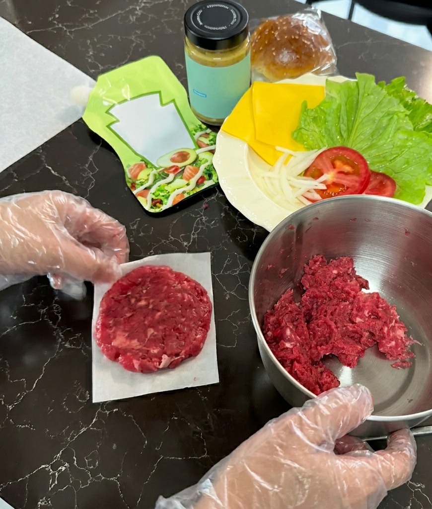 A raw beef patty flattened into a thin circle on a square of white parchment paper next to a bowl of ground meat.
