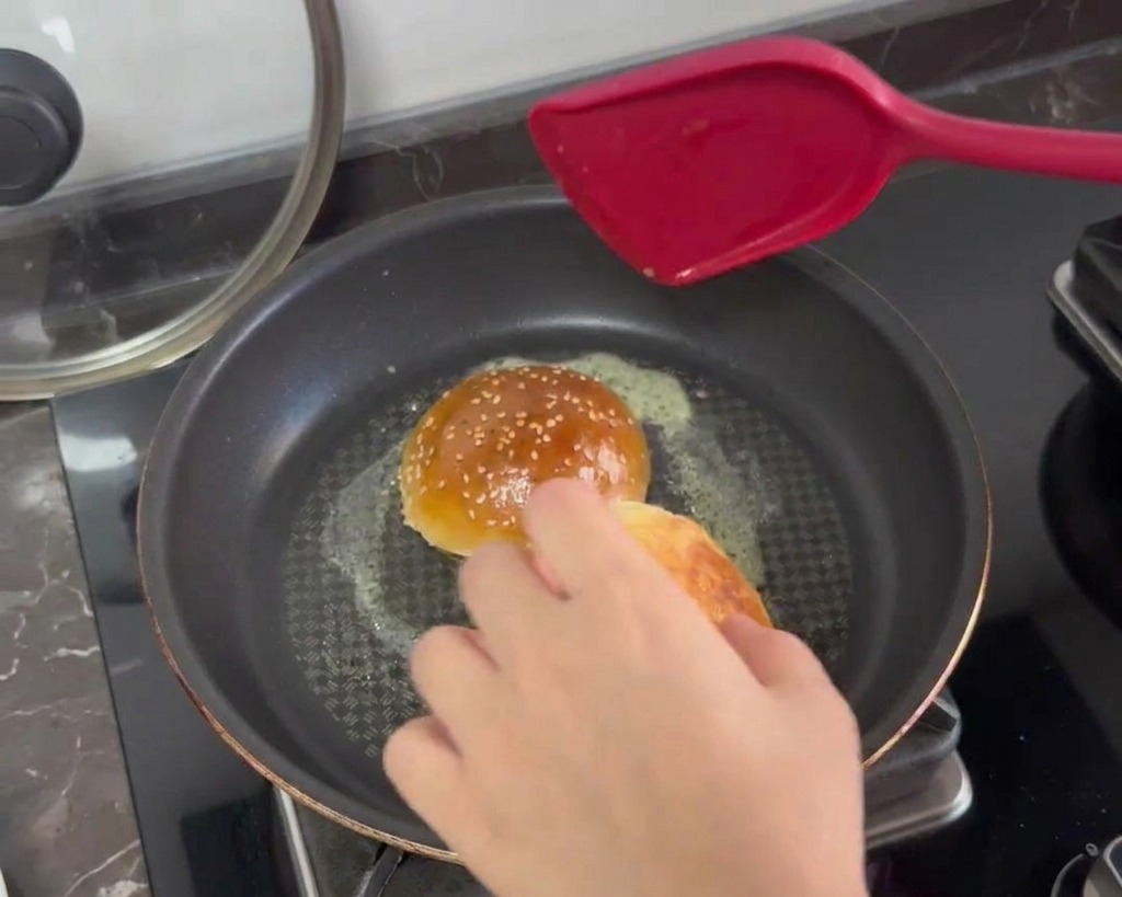 Burger bun halves being toasted face-down in a pan with bubbling melted butter.