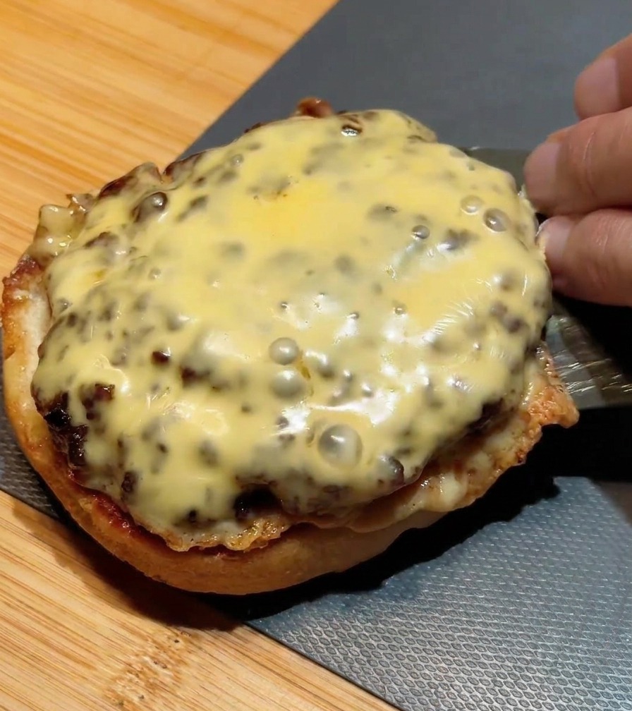 A metal spatula stacking a second seared beef patty with melted cheese onto a patty already on a bun.