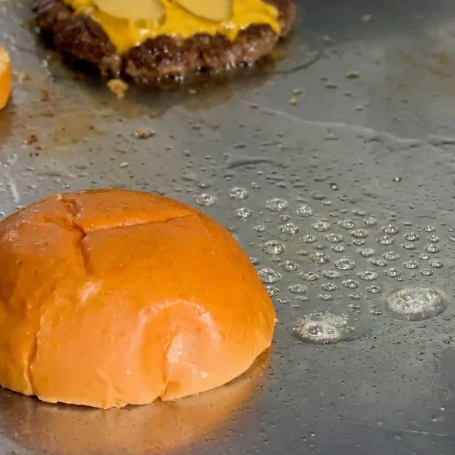 A brioche bun top being toasted on a griddle with fat bubbling around the edges.