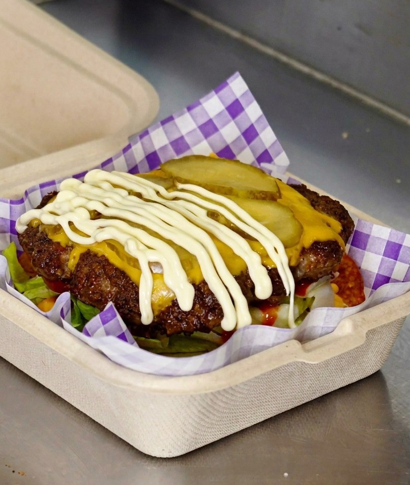 White mayonnaise being drizzled over pickle slices on a cheeseburger patty.