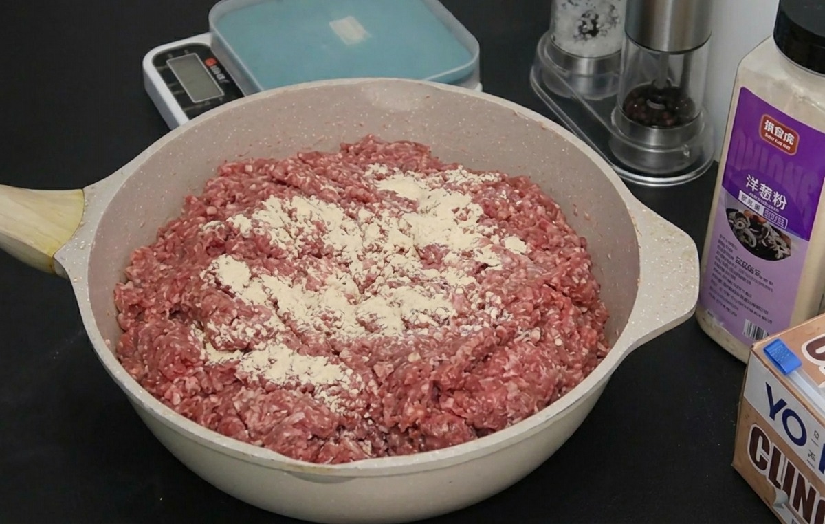 Raw ground beef in a pan with a fine layer of white onion and garlic powder seasoning on top.