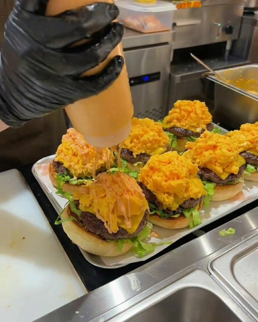 Orange burger sauce being squeezed over a tall pile of scrambled eggs on an assembled burger.