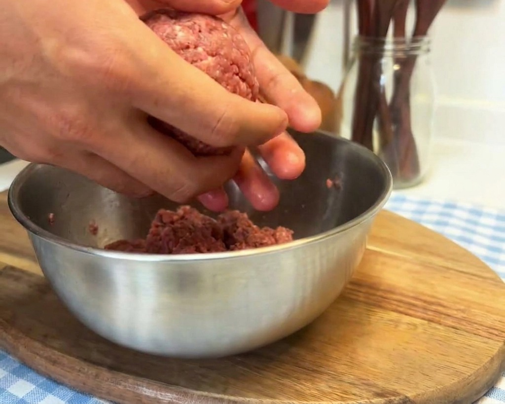 Hands working a ball of raw ground beef by slamming it into the palm to tighten the texture before shaping.