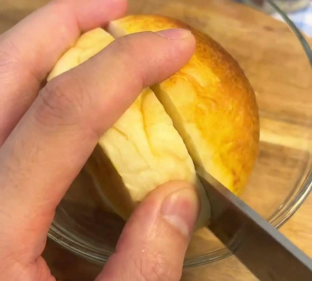 A serrated knife cutting through the middle of a perfectly toasted, golden-brown burger bun on a wooden surface.