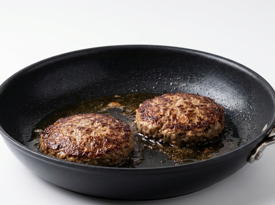Two seared beef patties flipped over in a pan, showing a crispy dark brown crust.