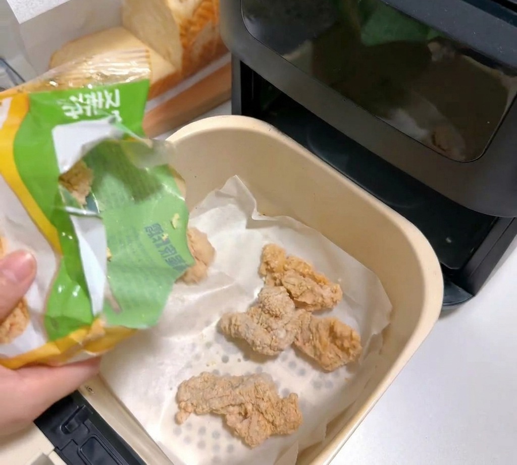 Frozen breaded chicken pieces being poured into a parchment-lined air fryer basket.