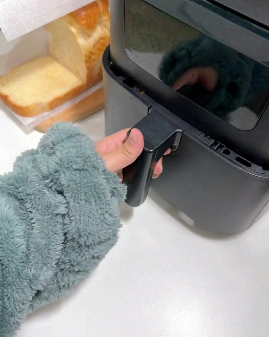 A hand in a fuzzy sleeve closing the drawer of a black air fryer.
