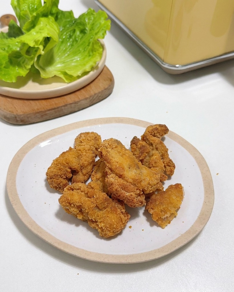 Crispy fried chicken pieces piled on a small white plate next to fresh lettuce leaves.