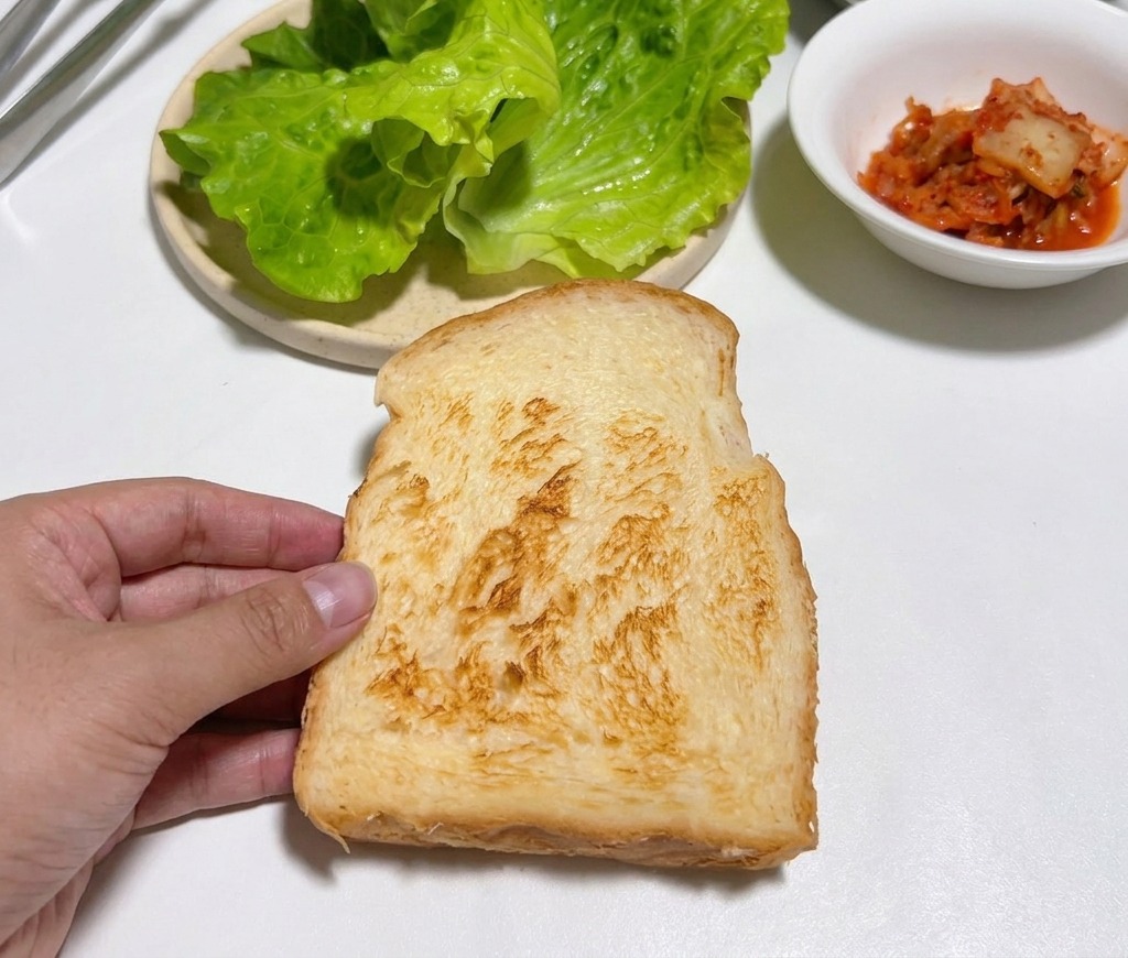A hand holding a golden brown slice of toasted bread over a white table.