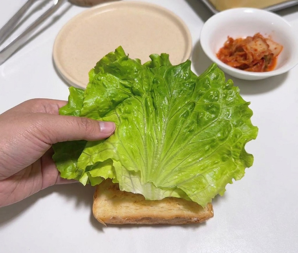 A hand placing a vibrant green lettuce leaf on a piece of toast on a white counter.