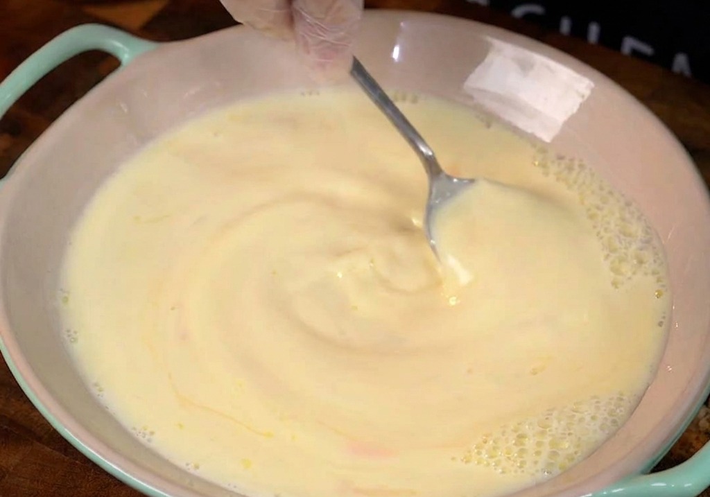 Milk and eggs with visible honey swirls being stirred in a light pink ceramic bowl.