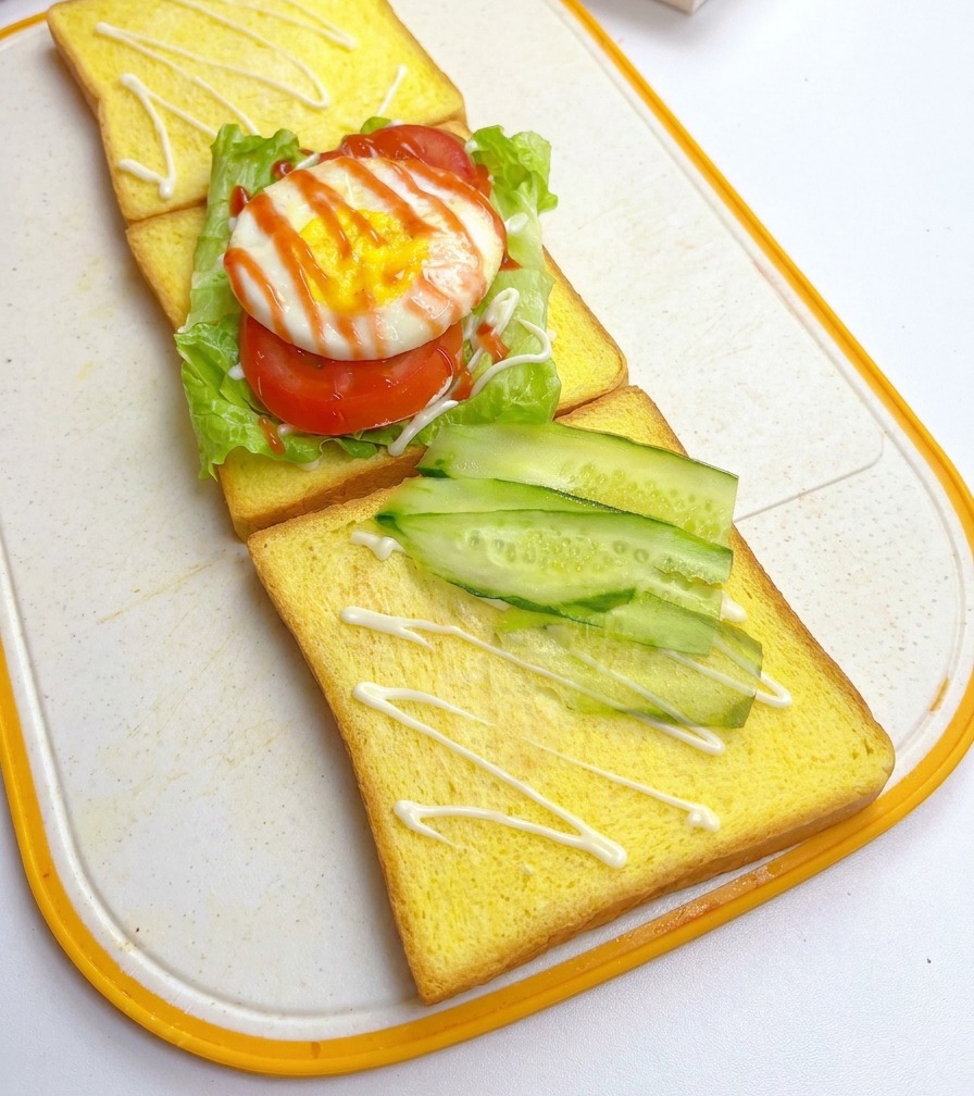 Thin slices of fresh cucumber arranged diagonally on a piece of yellow toast, positioned next to the first sandwich layer.