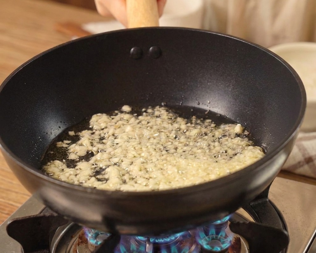 Minced garlic sizzling in oil at the bottom of a black wok over a blue gas flame.