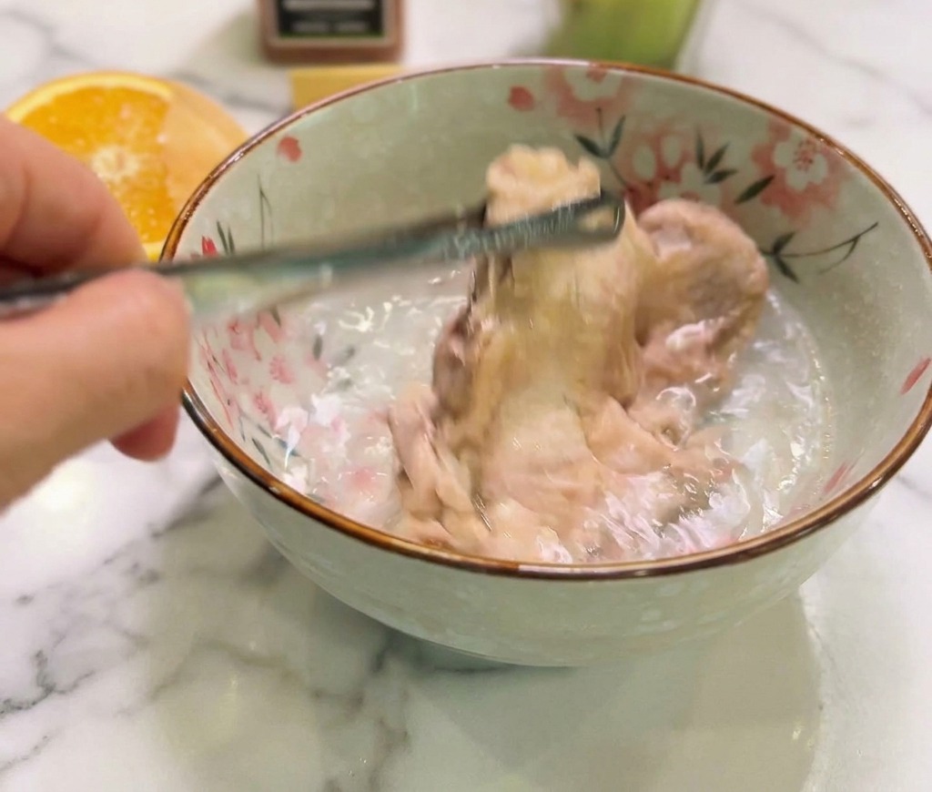 Cooked chicken being submerged into a floral-patterned ceramic bowl filled with clear cold water to stop the cooking process.