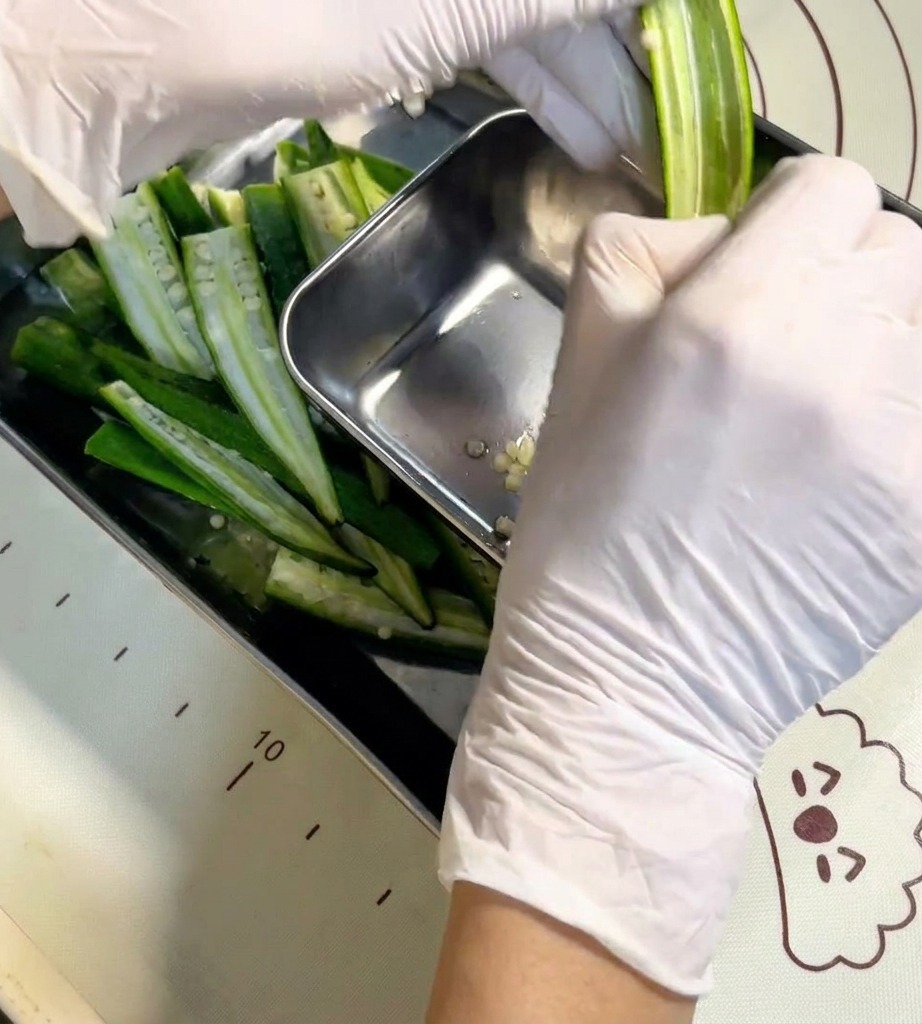 A hand using a small metal spoon to clean the seeds out of a split okra pod.