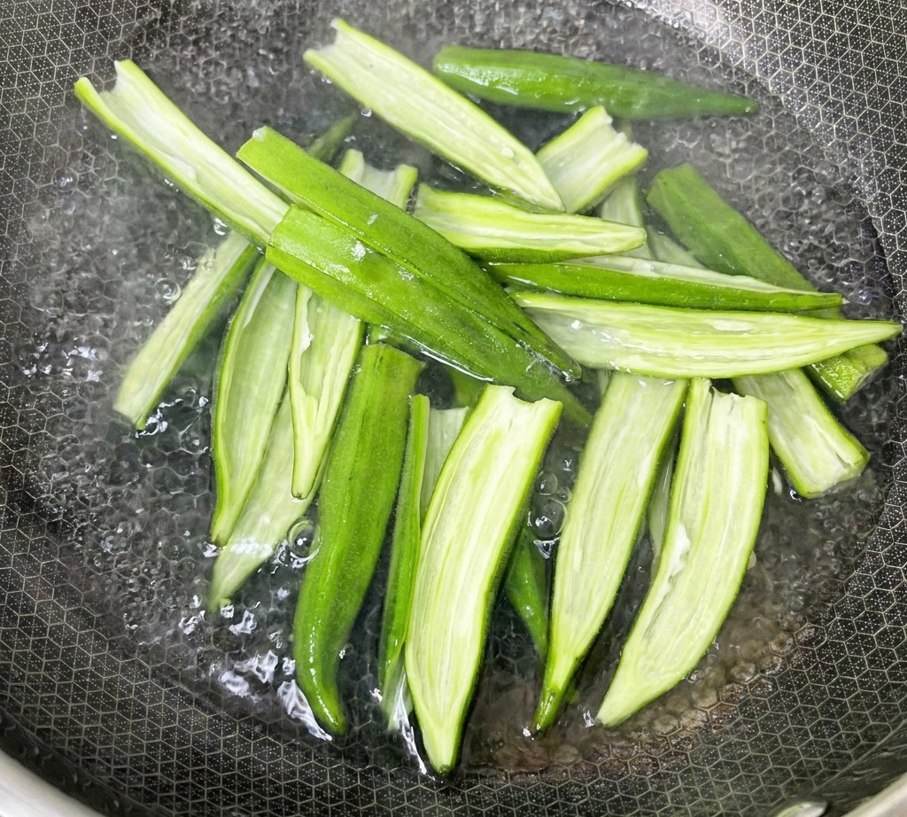 Split okra shells boiling in a pot of water on the stove.