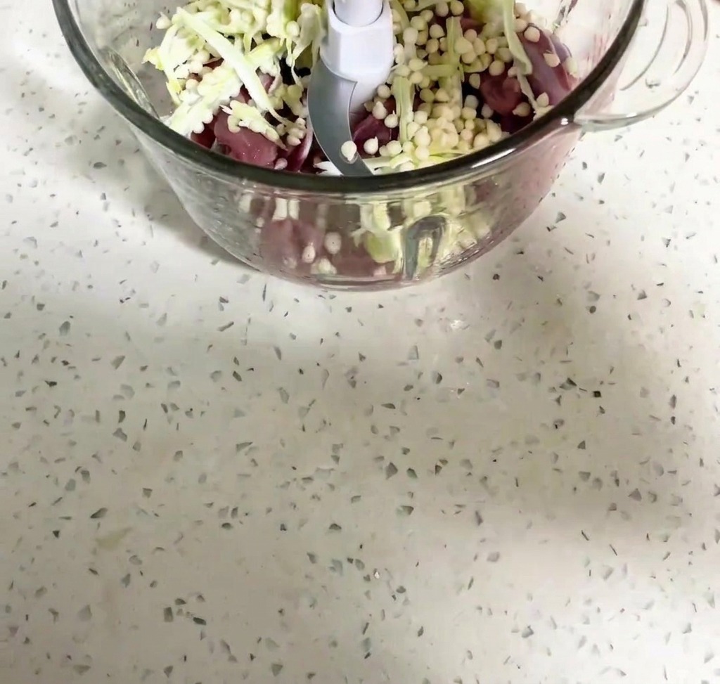Duck meat and okra seeds being blended inside a food processor bowl.