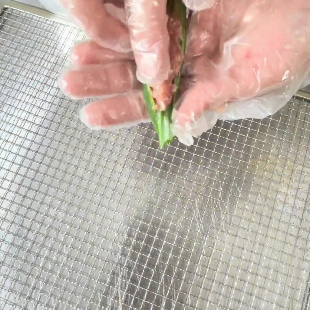 Hand in a food-safe glove stuffing the seasoned duck mixture into a halved okra pod.