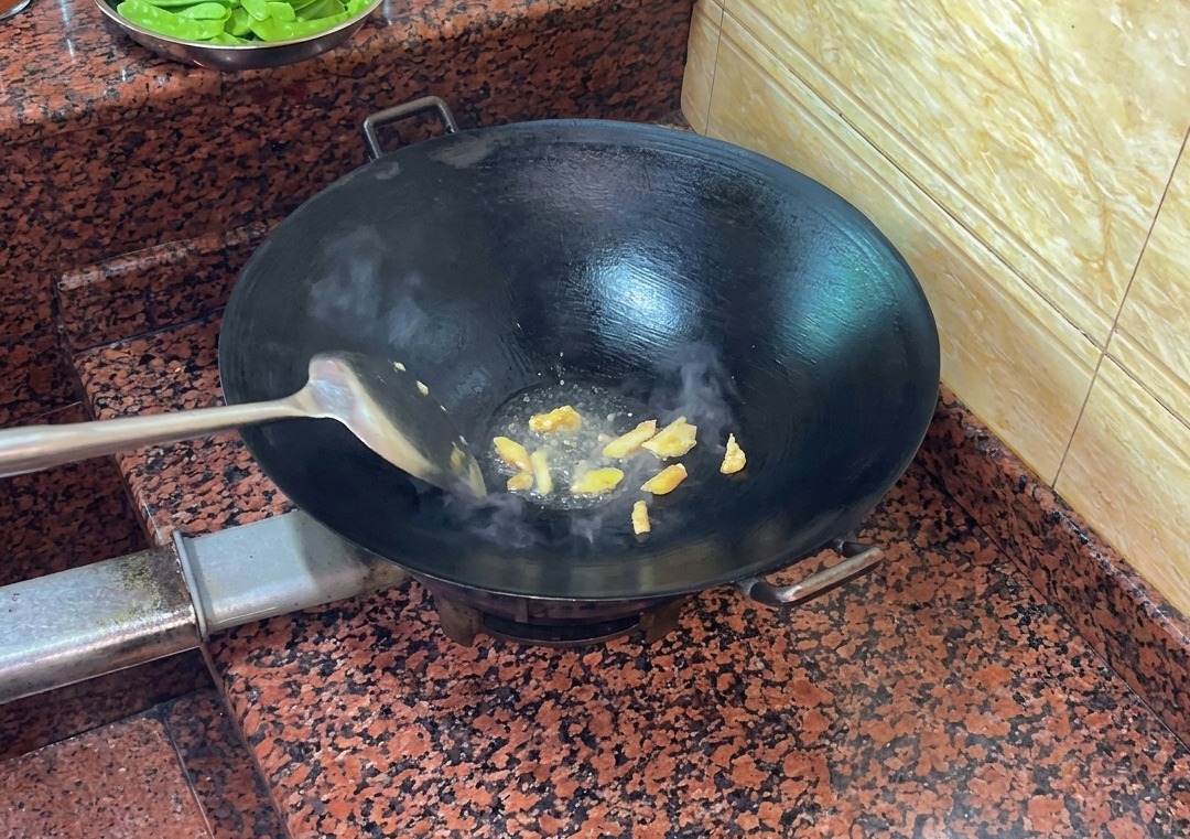 Duck skin pieces frying in a hot, dry wok, releasing liquid fat.