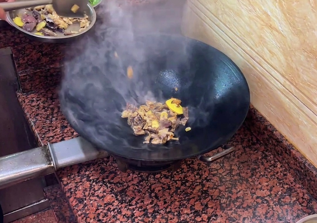 Duck liver sausage pieces stir-frying with aromatics in the wok.