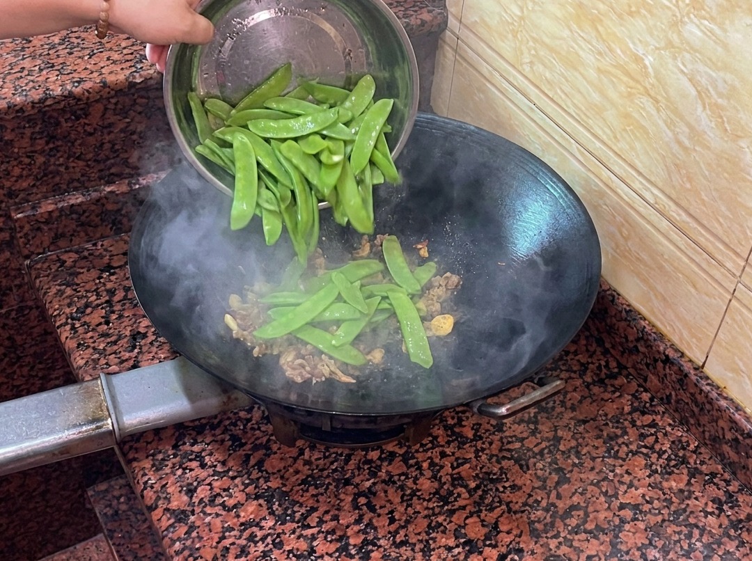 Fresh snow peas being added to the wok with the sausage and aromatics.