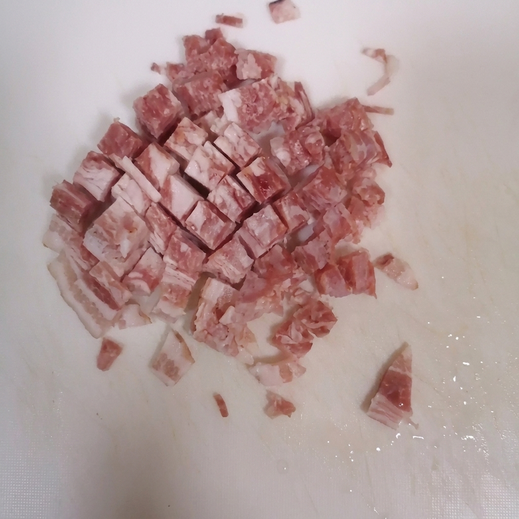 Bacon slices being cut into small cubes on a clean white cutting board.