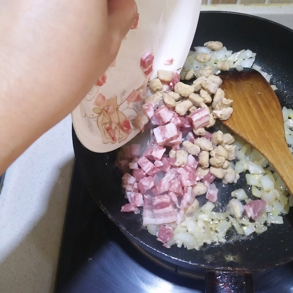 Diced bacon and beef cubes being stir-fried in a pan with onions and garlic.